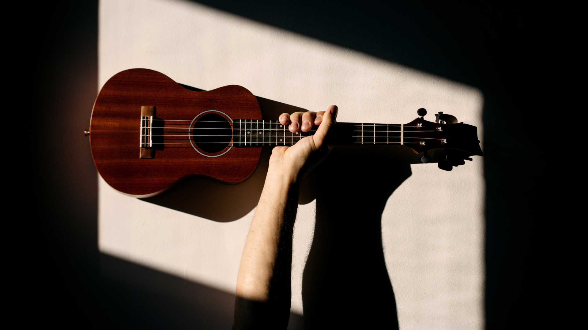 Drewniane ukulele na ścianie, na którą pada cień