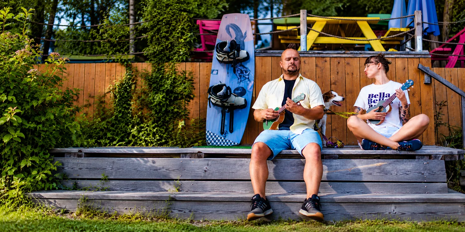 Dwoje ludzi grających na ukulele na drewnianym tarasie